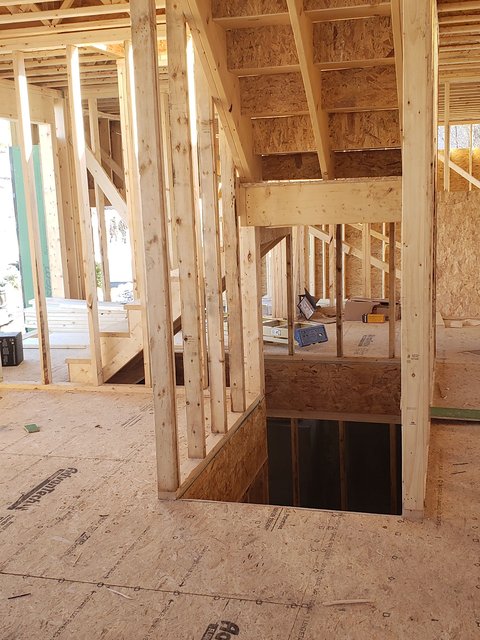 Interior of a new home with framed walls, an opening for the stairs in the subfloor and sunlight coming in through unfinished exterior walls